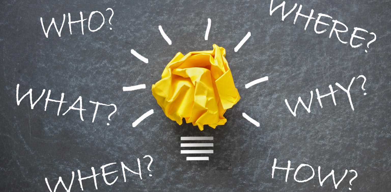 A scrunched up yellow paper forming part of a lightbulb concept with questions in white chalk on a grey surface