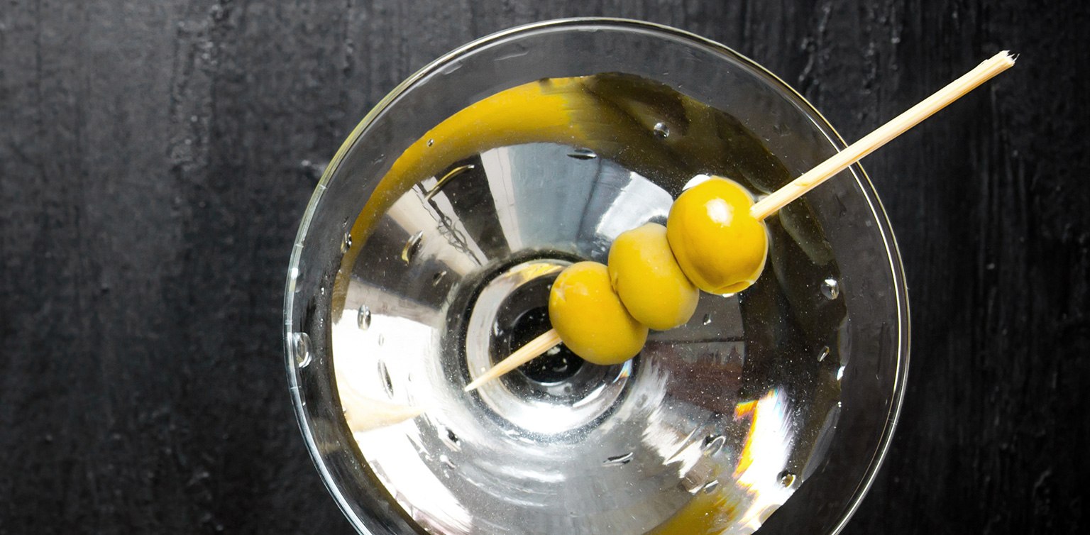 A photo of a martini cocktail garnished with three green olives, taken from above on a black table