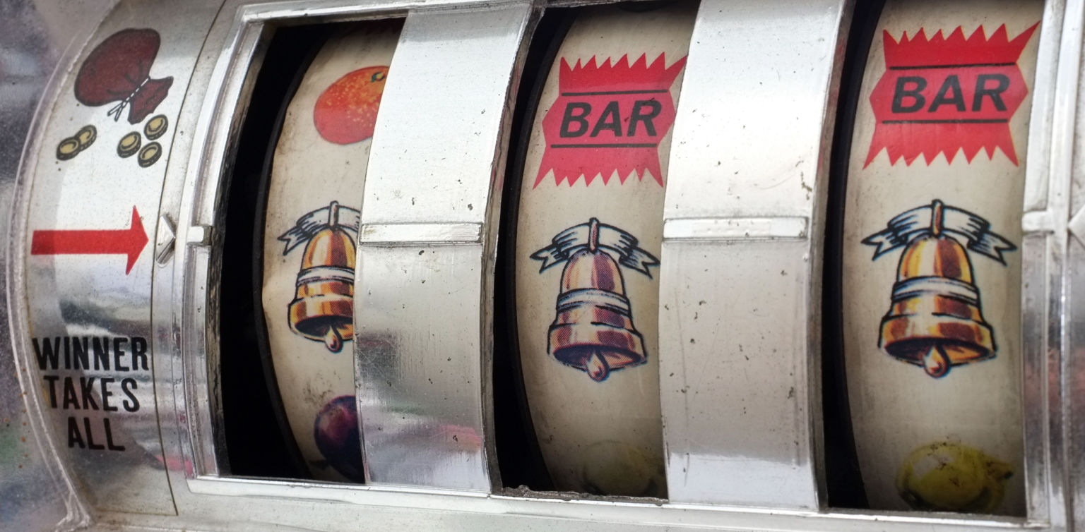 A close-up photo of an antique 3 reel slot barrel with bells, BARs and fruit symbols
