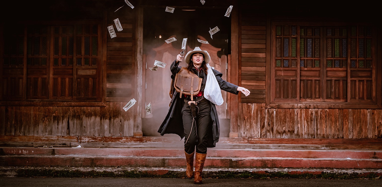 A photo of a cowgirl walking out of a bank with a bag of cash and money flying around after a successful heist