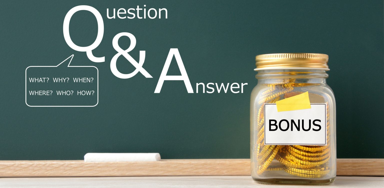 A glass jar with a ‘bonus’ label filled with gold coins on a wooden surface in front of a green chalk board with 'Q&A' on it