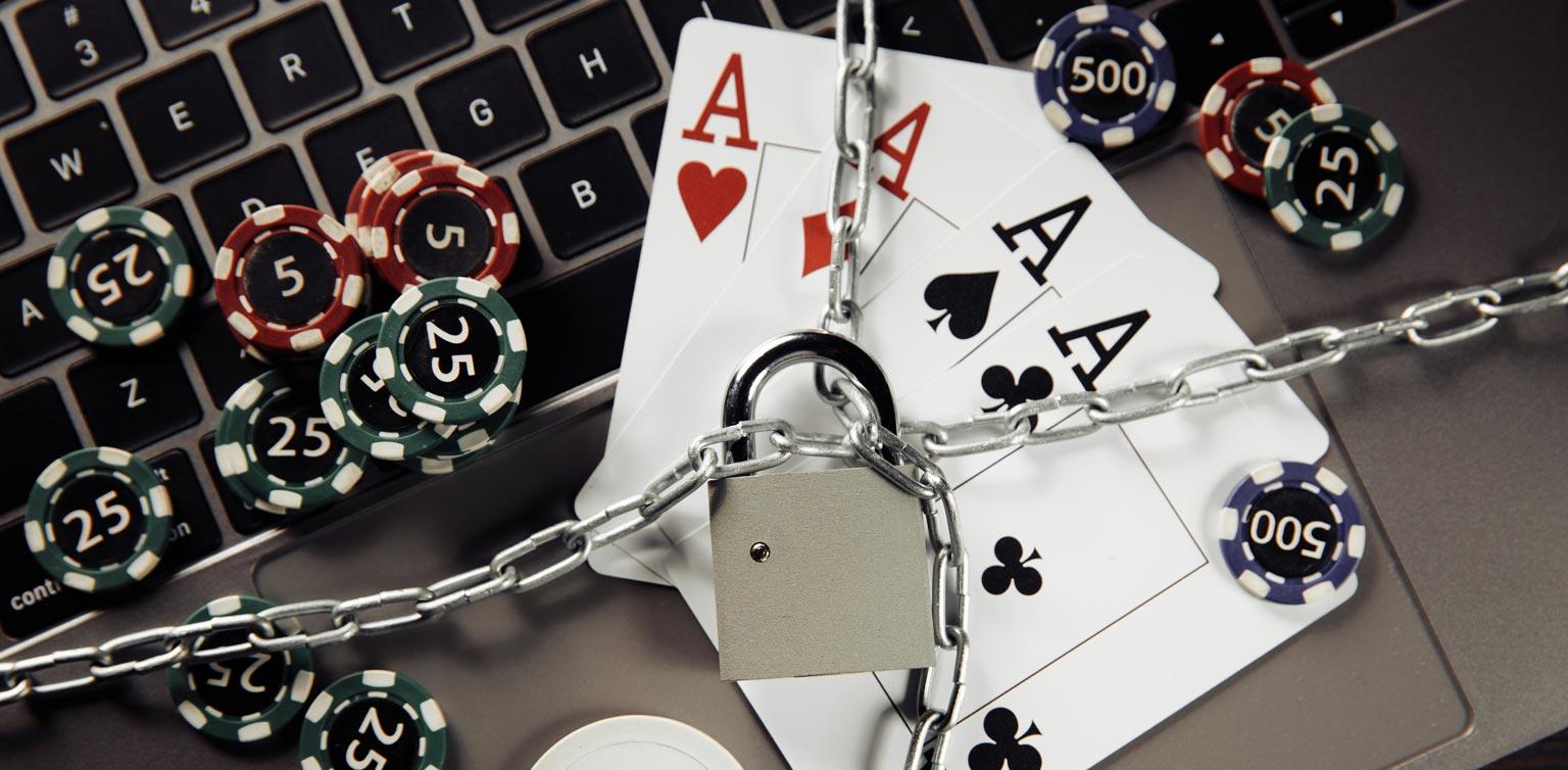 A close-up image of a laptop with playing cards and poker chips on with chains and a padlock