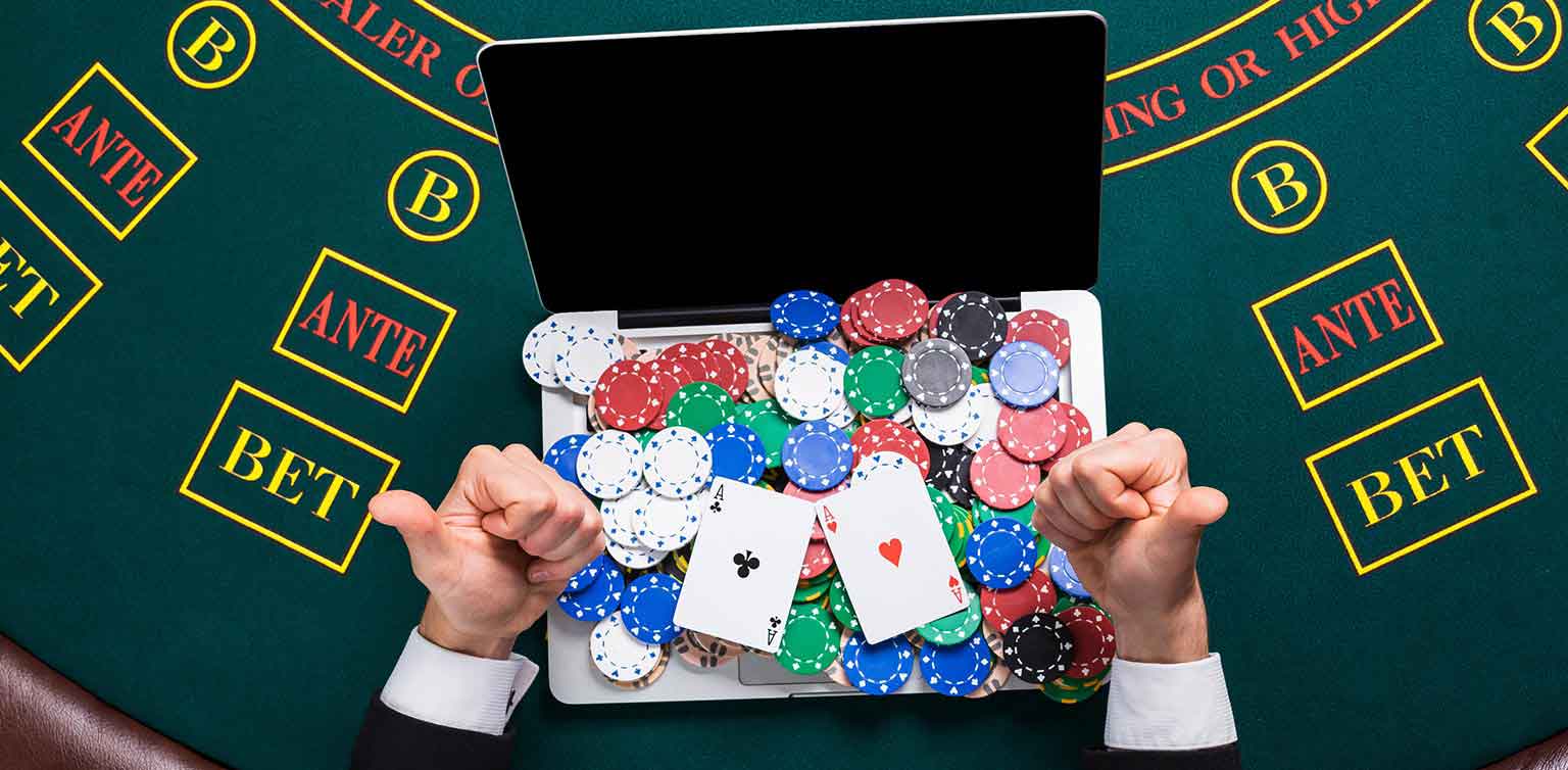 An image of a man making two thumbs up gestures sitting at a blackjack table with a laptop with stacks of poker chips on